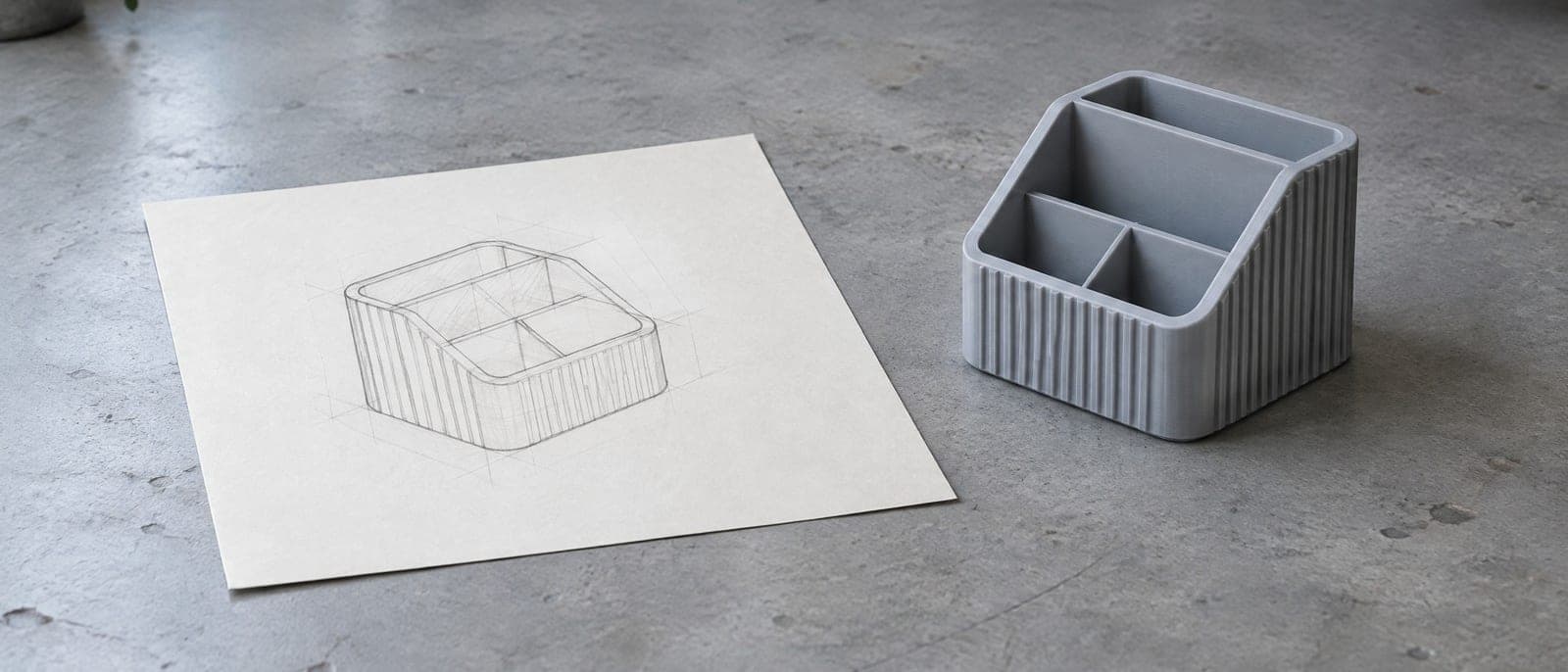 Een potloodschets van een bureau-organizer op papier, met rechts ernaast dezelfde organizer als grijze 3D-print.