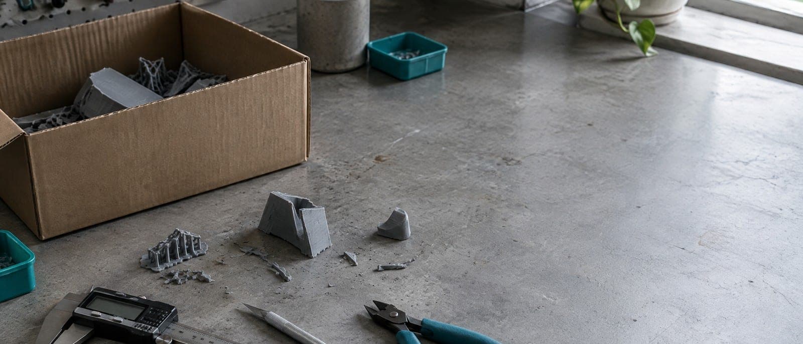 Een betonnen werkblad met een schuifmaat, een hobbymes, een zijkniptang en een kartonnen doos met afgeknipte supports.